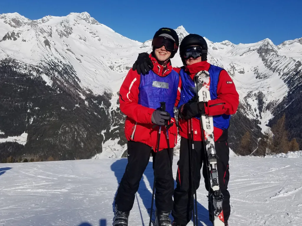 Zwei Personen stehen auf Skiern vor der Bergkulisse.